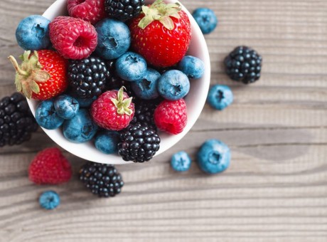 Fresh berries in a basket on rustic wooden background.